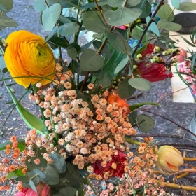 Blumenstrauß in einer Hand, Gelbe Ranunkel, Tulpen in verschiedenen Farben,
Eukalyptus, Statice oder getrocknetes Schleierkraut, Rote Nelken