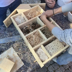 Person füllt Insektenhotel mit Naturmaterialien, eine Schüssel mit Lehm steht daneben