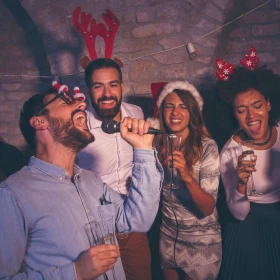 Personen singen gemeinsam einen Karaoke Song mit weihnachtlichen Mützen