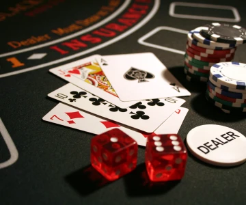 Spielkarten, 2 rote Würfel, Pockerchips und ein Chip mit der Aufschrift "Dealer" liegen auf einem Casinotisch