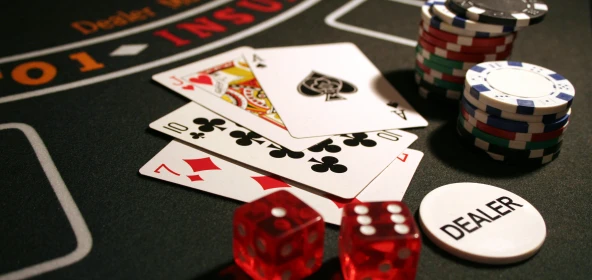 Spielkarten, 2 rote Würfel, Pockerchips und ein Chip mit der Aufschrift "Dealer" liegen auf einem Casinotisch