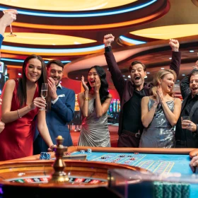 Gruppe steht vor einem Roulette Tisch und sie freuen sich
