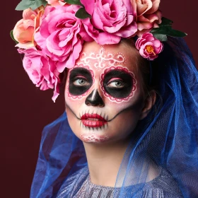 eine junge Frau verkleidet und im Gesicht geschminkt für den mexikanisches Tag der Toten vor einem roten Hintergrund