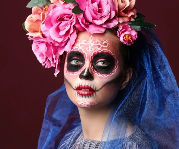 eine junge Frau verkleidet und im Gesicht geschminkt für den mexikanisches Tag der Toten vor einem roten Hintergrund