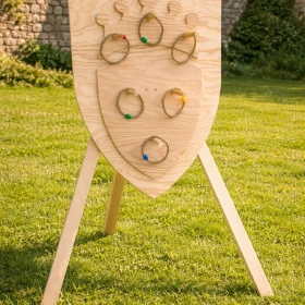 Dieses Bild zeigt ein mittelalterliches Geschicklichkeitsspiel mit Holzschild und Ringwurf-Element.  Ideal zur Darstellung interaktiver Spielstationen auf einem Ritterturnier.