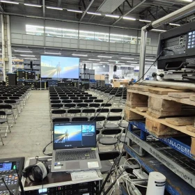 Beamer und Laptop mit einer Leinwand in einer Halle mit Stühlen